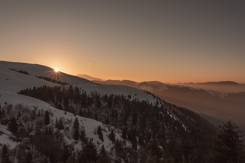 the sun is setting over a snowy mountain