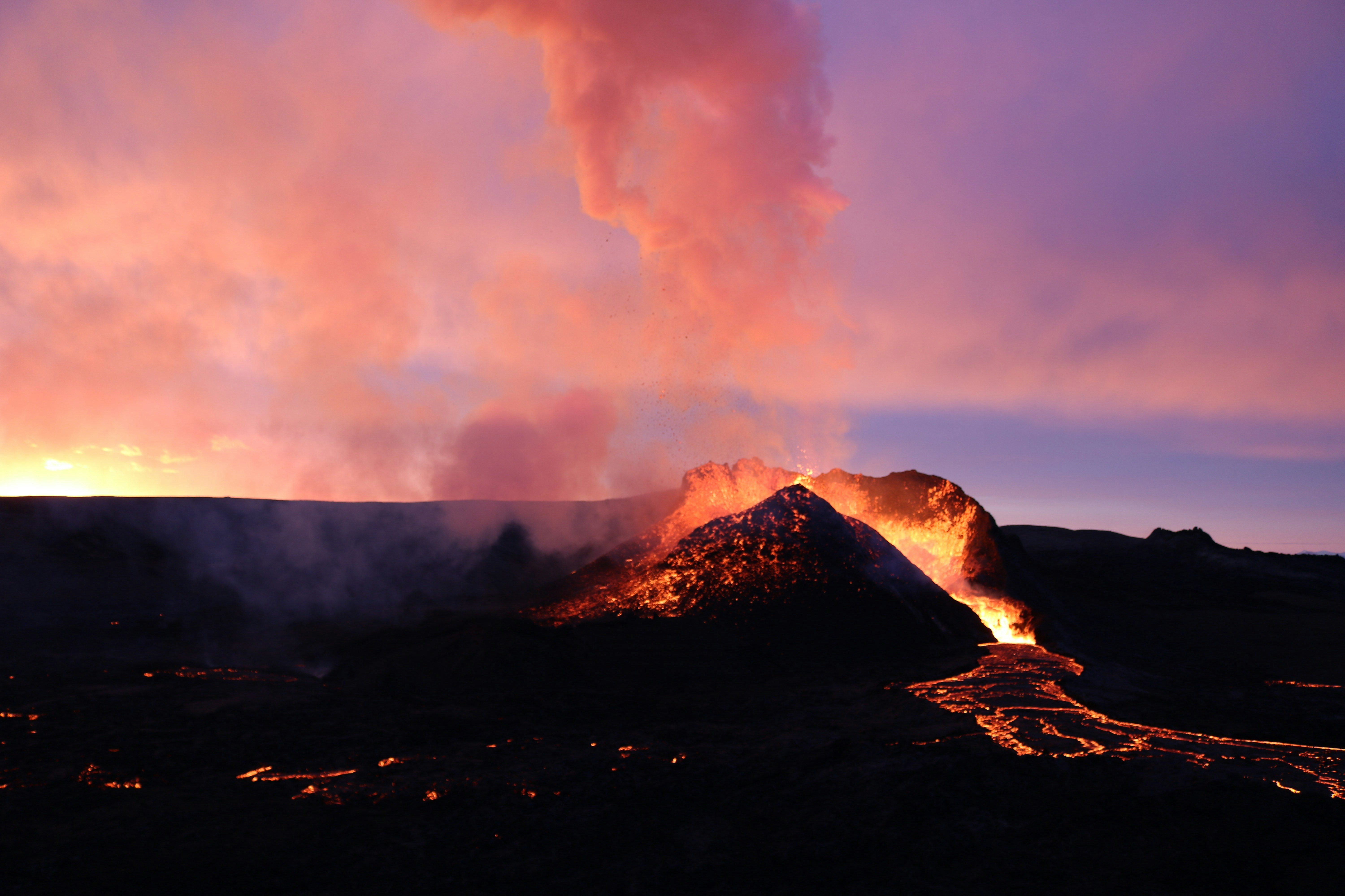 a volcano erupts lava as the sun sets, 