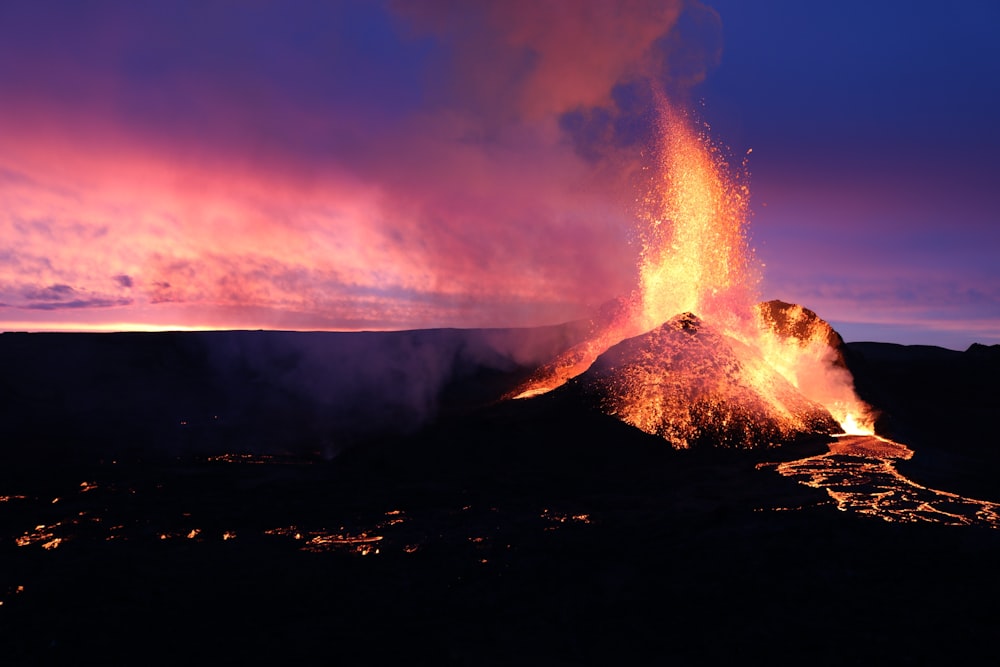 a volcano erupts lava as the sun sets