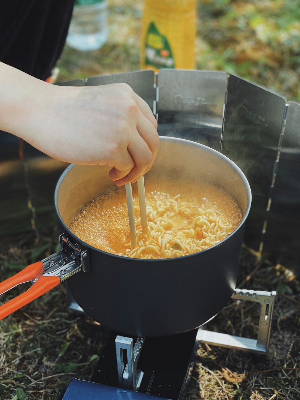 a person stirring a pot of noodles with chopsticks