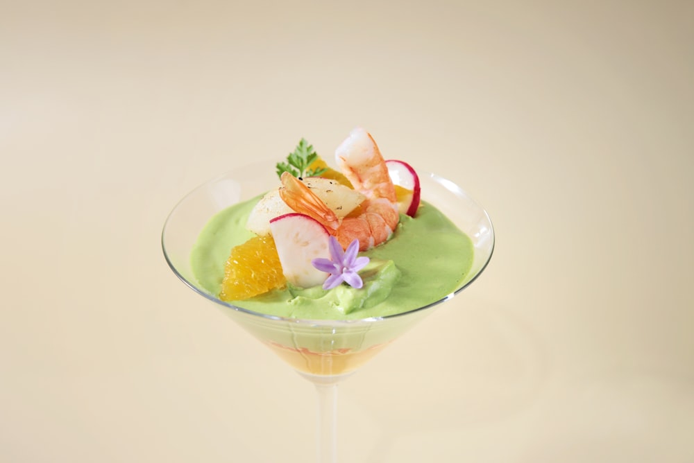 a glass filled with a green dessert and garnished with fruit