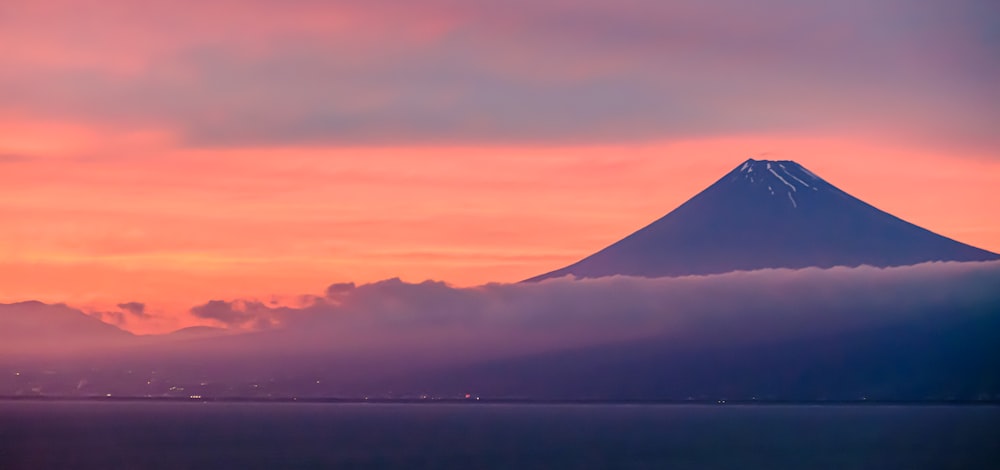 a mountain covered in clouds and a pink sky