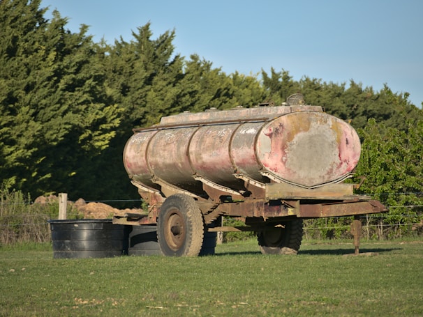 A sleek oil tank trailer parked beside a refinery under a clear sky