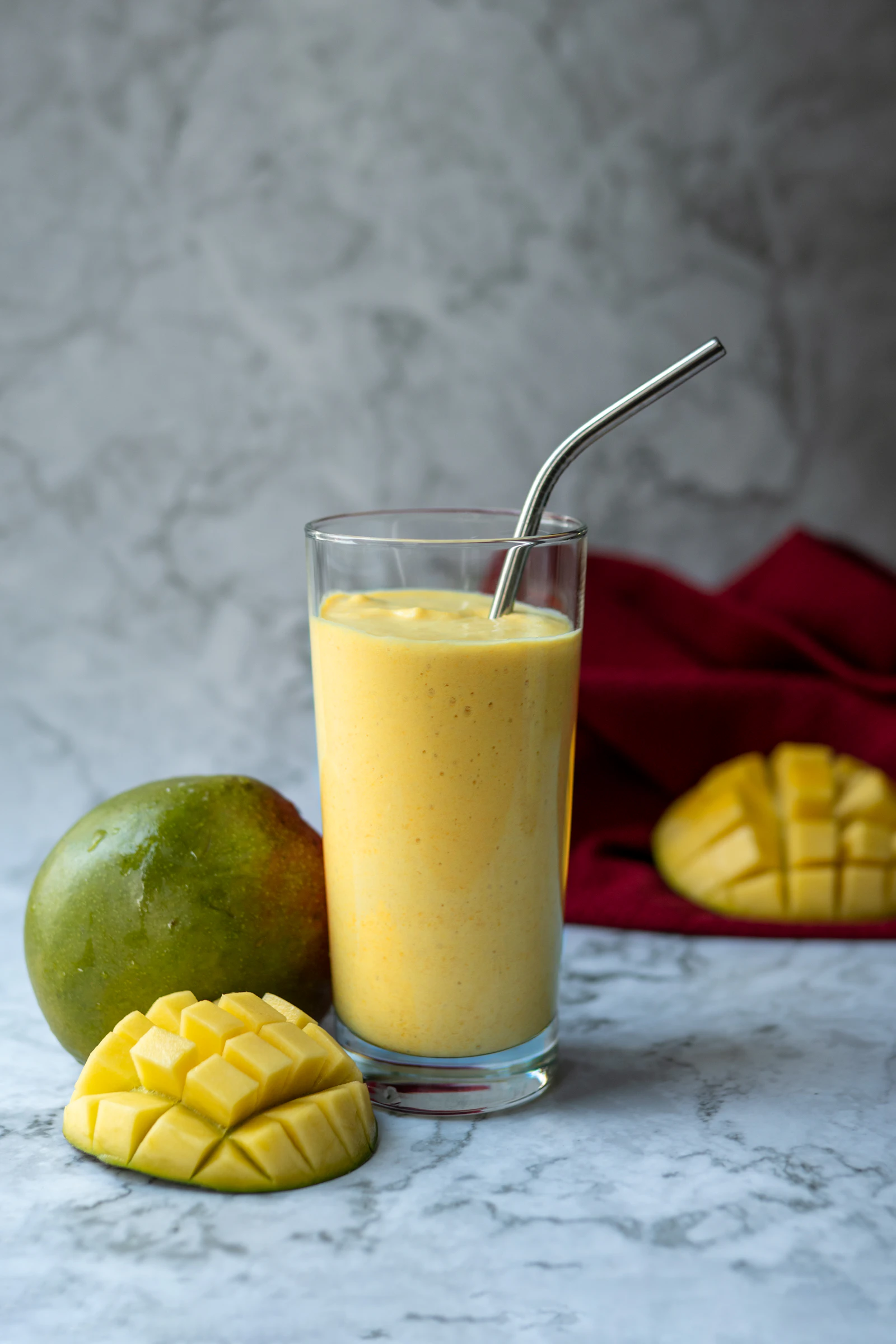 A tall glass of blended mango smoothie garnished with fresh mango