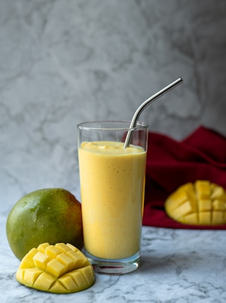 a glass filled with a smoothie next to a mango