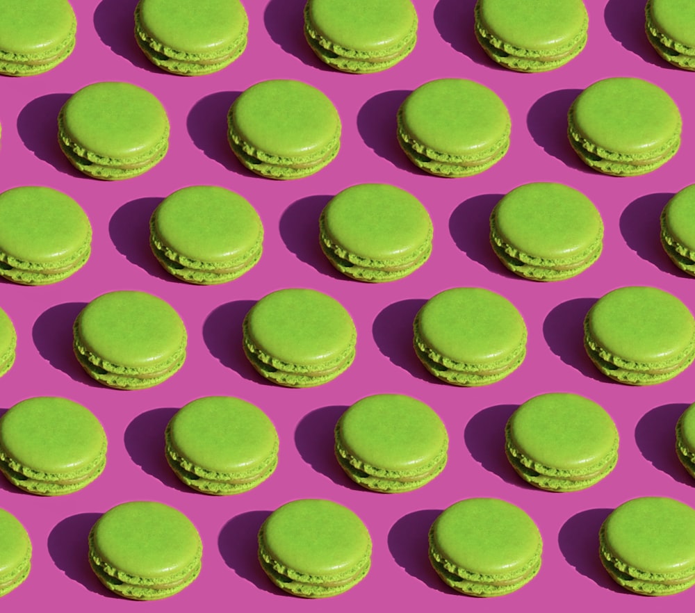 green macaroons are arranged in rows on a pink background