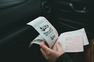 A person is holding and examining what appears to be lottery tickets inside a car. The image is focused on the tickets and the person's hands, with parts of the car interior visible in the background.