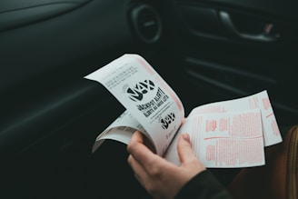 A person is holding and examining what appears to be lottery tickets inside a car. The image is focused on the tickets and the person's hands, with parts of the car interior visible in the background.