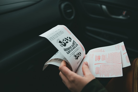 A person is holding and examining what appears to be lottery tickets inside a car. The image is focused on the tickets and the person's hands, with parts of the car interior visible in the background.