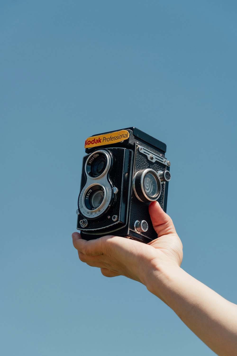 a hand holding an old fashioned camera in front of a blue sky