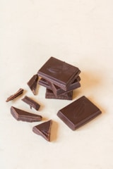 Several pieces of dark chocolate, some whole and some broken, are arranged on a light surface. The chocolate bars feature an embossed design.