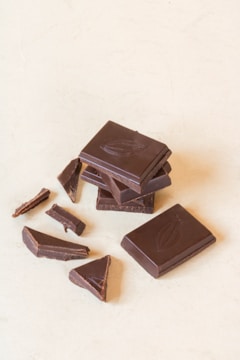 Several pieces of dark chocolate, some whole and some broken, are arranged on a light surface. The chocolate bars feature an embossed design.