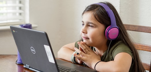 a little girl sitting at a table with a laptop