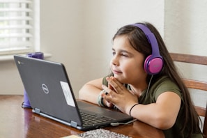 a little girl sitting at a table with a laptop