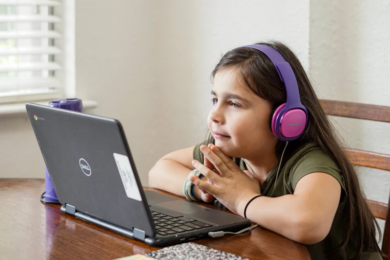 A young student smiling while writing code on a laptop in a bright classroom