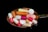A variety of colorful pills and capsules rest on a metallic spoon against a black background, creating a stark contrast. The pills are of different shapes and sizes, including round tablets and elongated capsules in hues of pink, orange, white, and green.