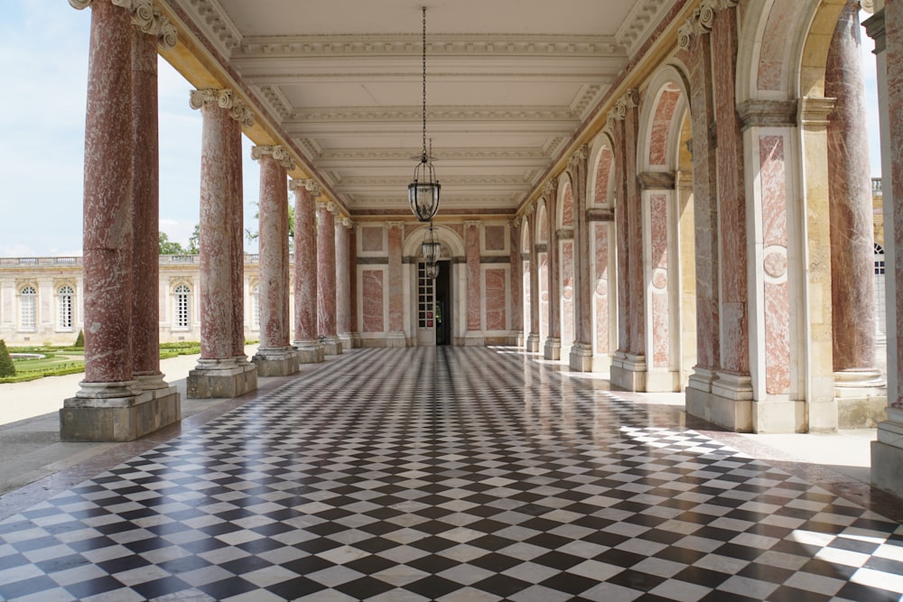 um longo corredor com colunas e um piso quadriculado
