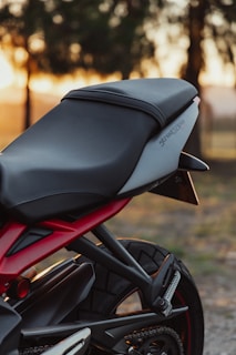 A sleek motorcycle seat with a modern design is pictured, featuring a black and grey color scheme. The backdrop includes a soft-focus view of trees and a sunset, creating a warm ambiance.