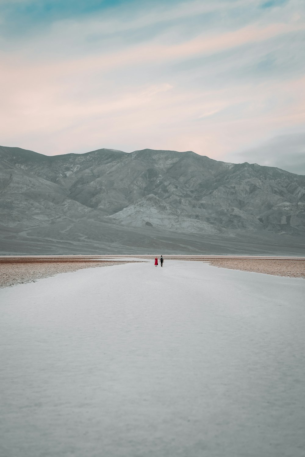person walking on brown sand near lake and mountains during daytime