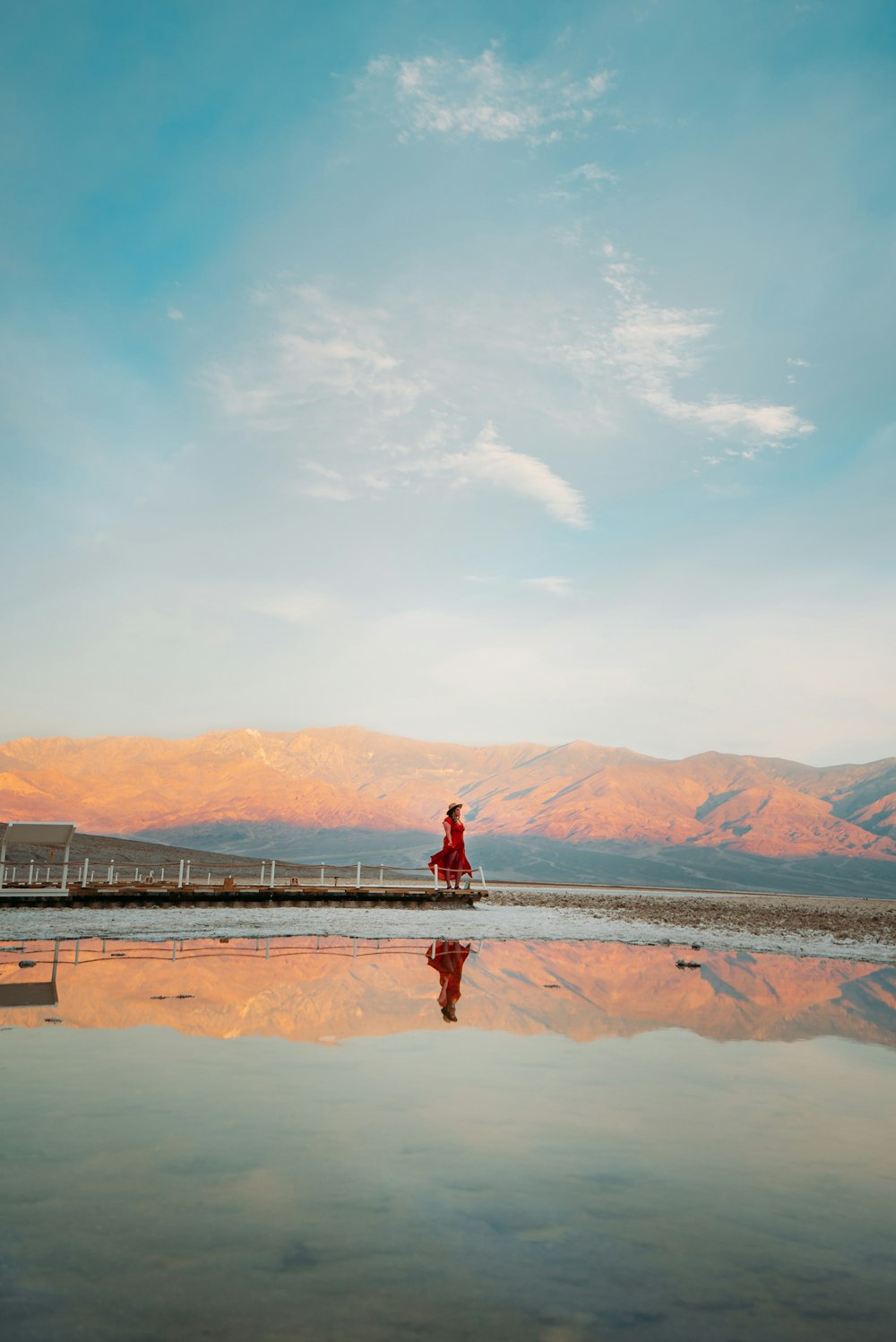pessoa em jaqueta vermelha em pé na areia marrom perto do corpo de água durante o dia