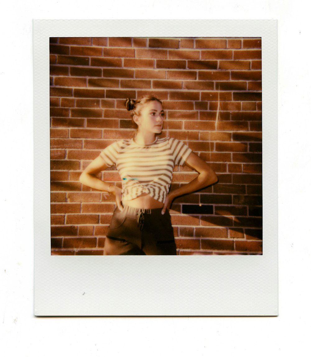 woman in black and white stripe tank top and black denim jeans leaning on brick wall