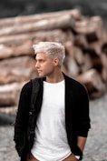 a man with white hair standing in front of a pile of logs