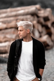 a man with white hair standing in front of a pile of logs