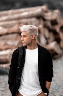 a man with white hair standing in front of a pile of logs