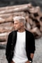 a man with white hair standing in front of a pile of logs