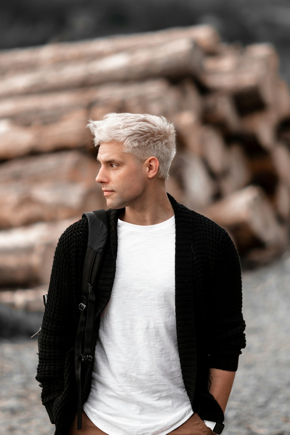 a man with white hair standing in front of a pile of logs
