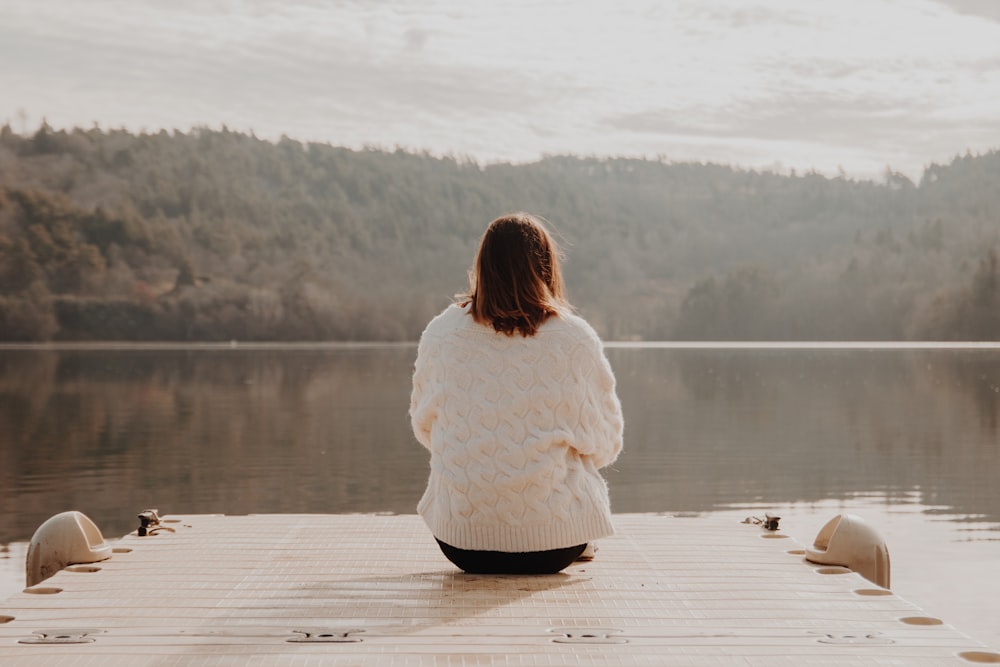 woman in white long sleeve shirt sitting on brown wooden dock during daytime