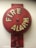 A red fire alarm bell mounted on a wall. The bell is circular with the words 'FIRE ALARM' written in bold, white letters. It has a weathered appearance with some faded and chipped paint.