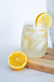 A refreshing drink being poured into a glass with ice and lemon.