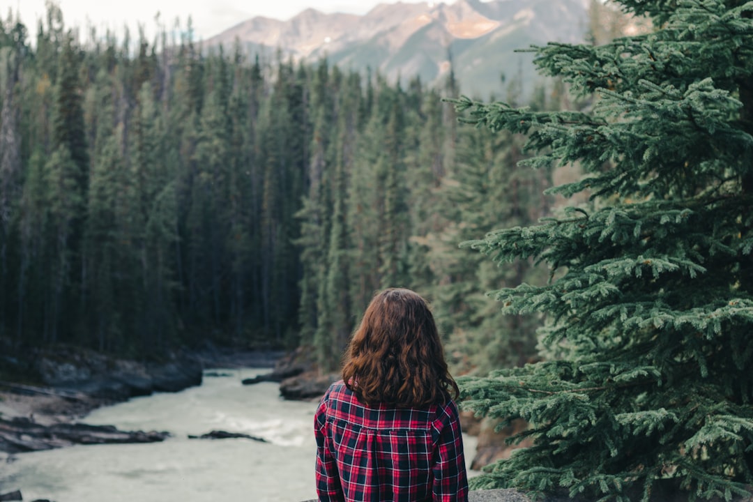 woman in red and black plaid shirt standing in front of green pine trees during daytime