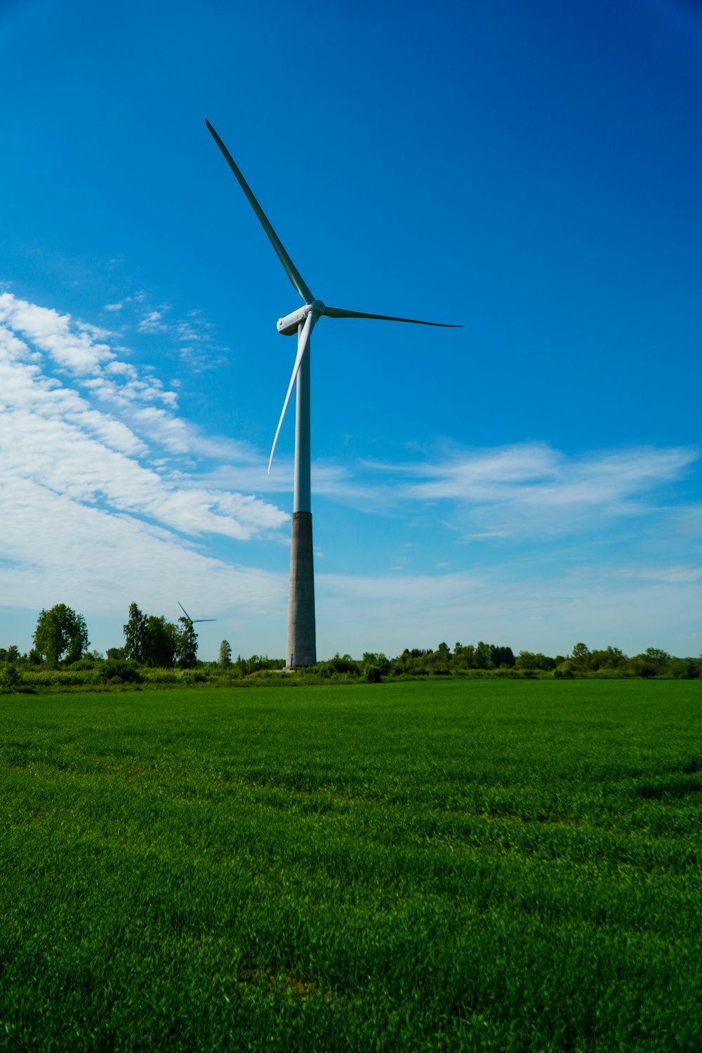 white wind turbine on green grass field under blue sky during daytime