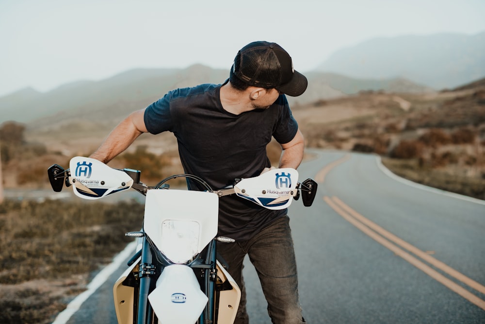 Homme en t-shirt noir roulant sur une moto bleue et blanche pendant la journée