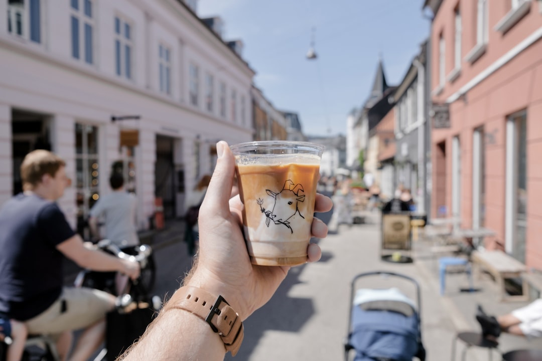 person holding clear glass cup with brown liquid,