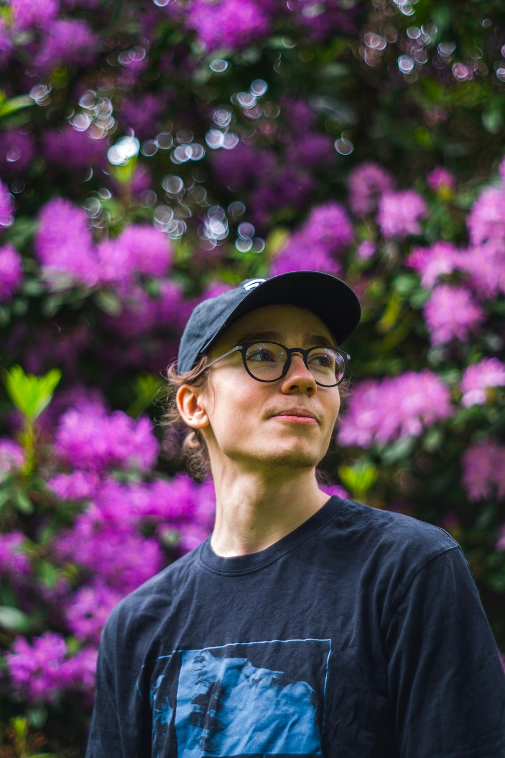 man in black crew neck shirt wearing black framed eyeglasses and black hat standing near purple