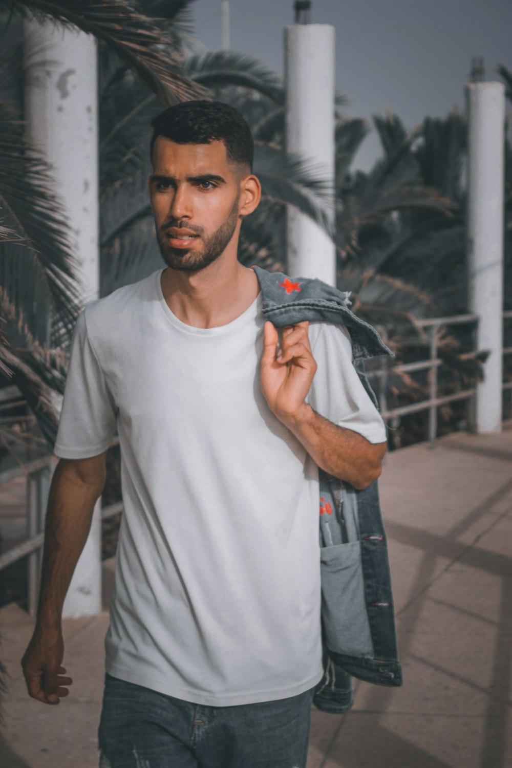 a man walking down a sidewalk carrying a jacket