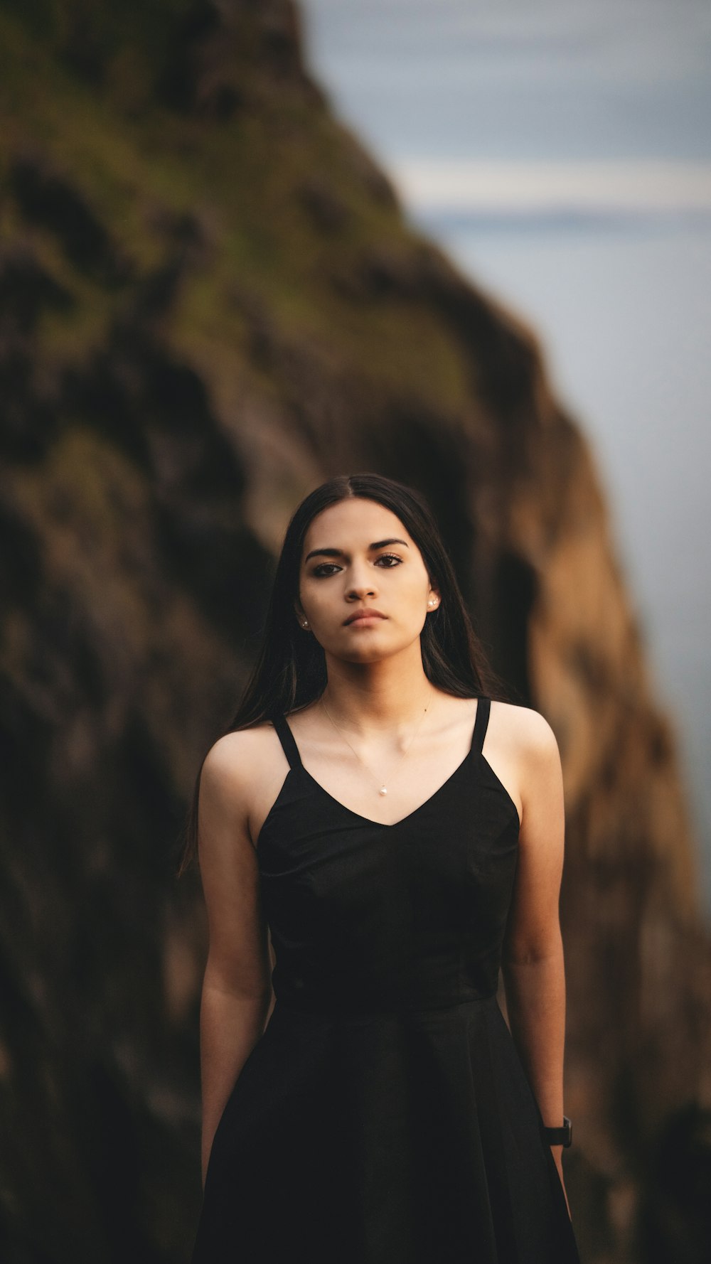 a woman in a black dress standing in front of a cliff