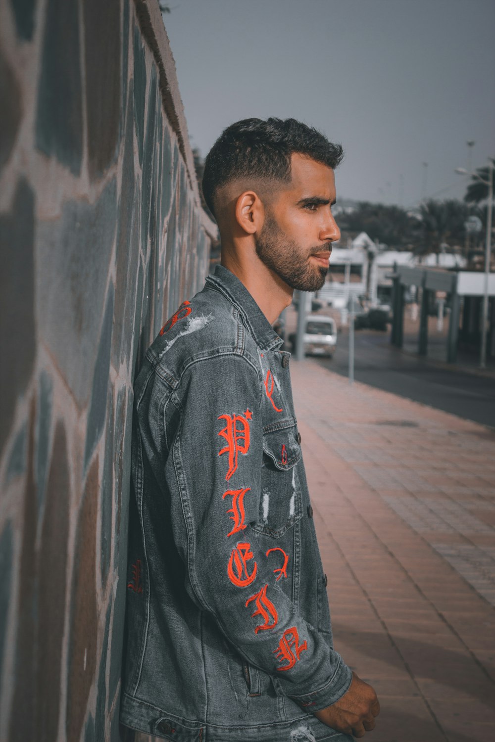 a man leaning against a wall wearing a jean jacket