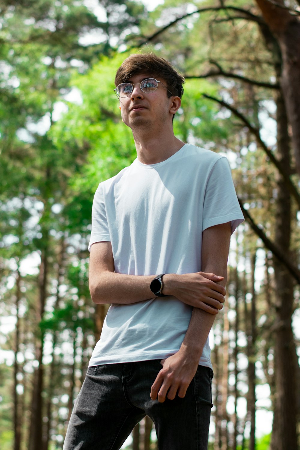 man in white crew neck t-shirt and black sunglasses standing near green trees during daytime