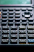 Close-up view of a calculator with numerous buttons, including numbers, arithmetic operations, and special functions like EXP and EXE. The keys are dark in color, with white labels, and the surface has a slightly worn appearance.