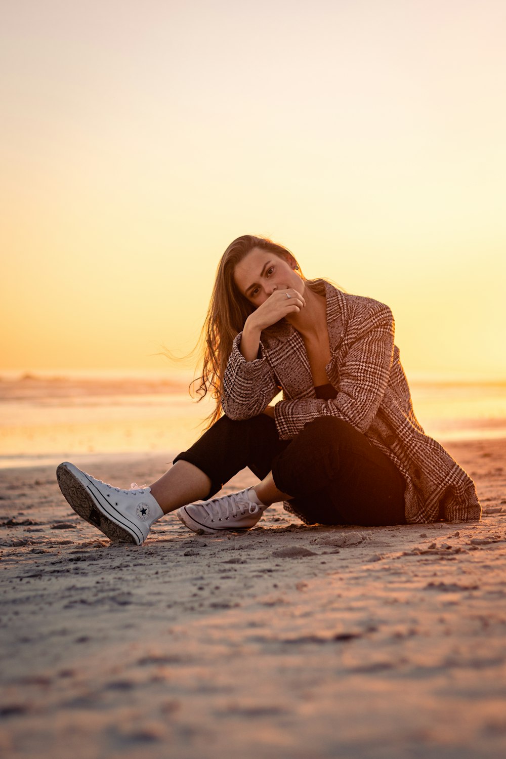 a woman sitting on the beach at sunset