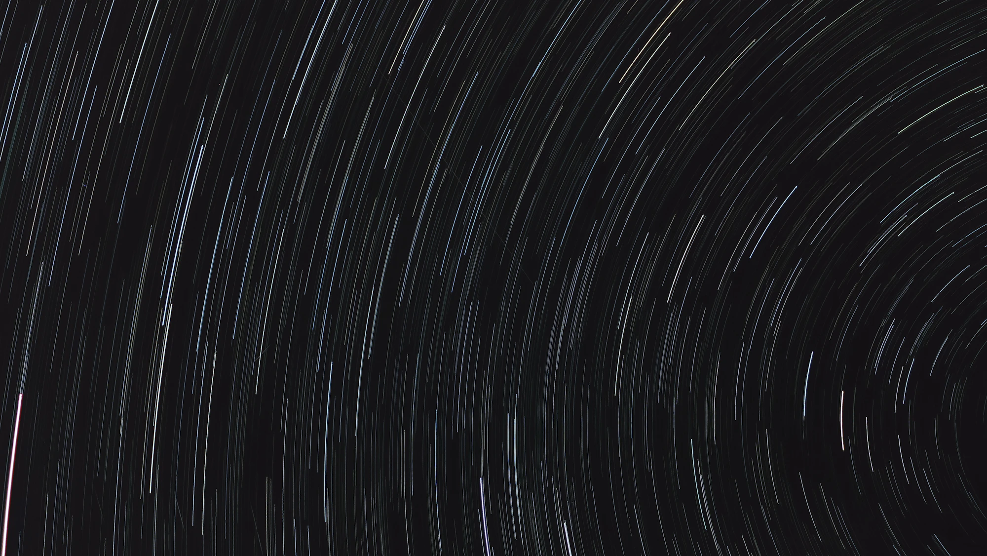 Circular star trails curving around a point in a dark night sky above a silhouetted landscape.