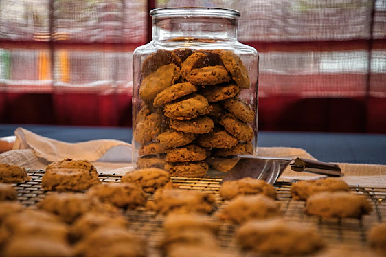 A warm kitchen scene showing freshly baked cookies cooling on a rustic wooden table with honey jars nearby.