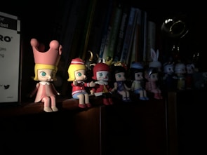 A group of ceramic anime figurines arranged on a wooden shelf with soft lighting.