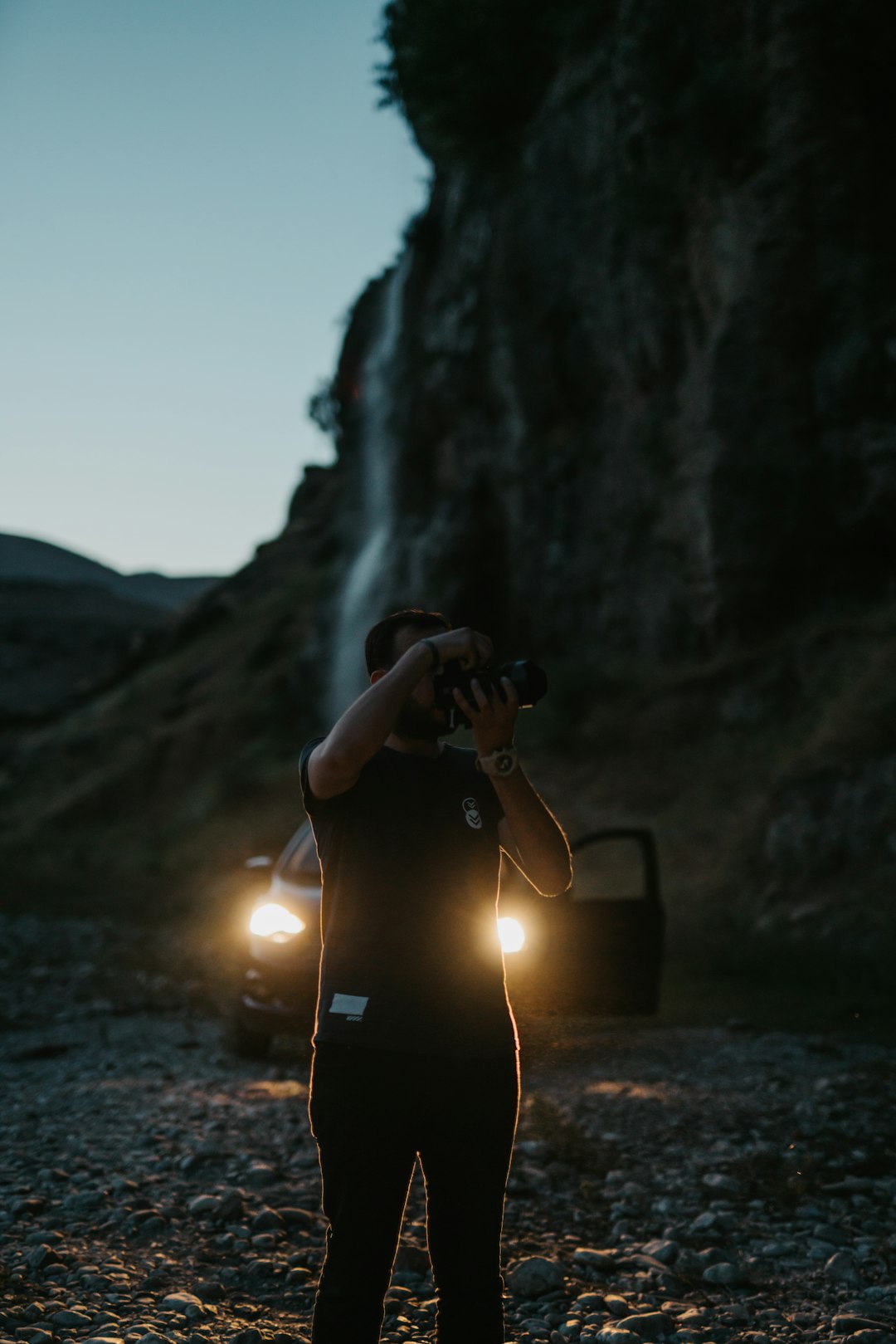 person in black jacket sitting on rock near waterfalls during daytime