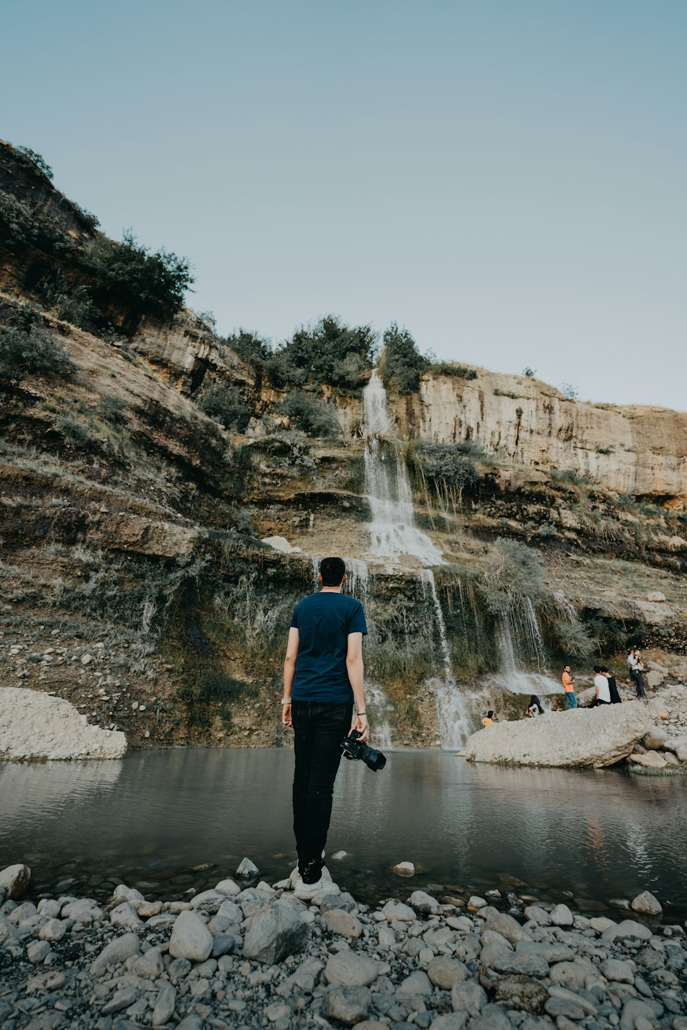 man in black pants standing near waterfalls during daytime