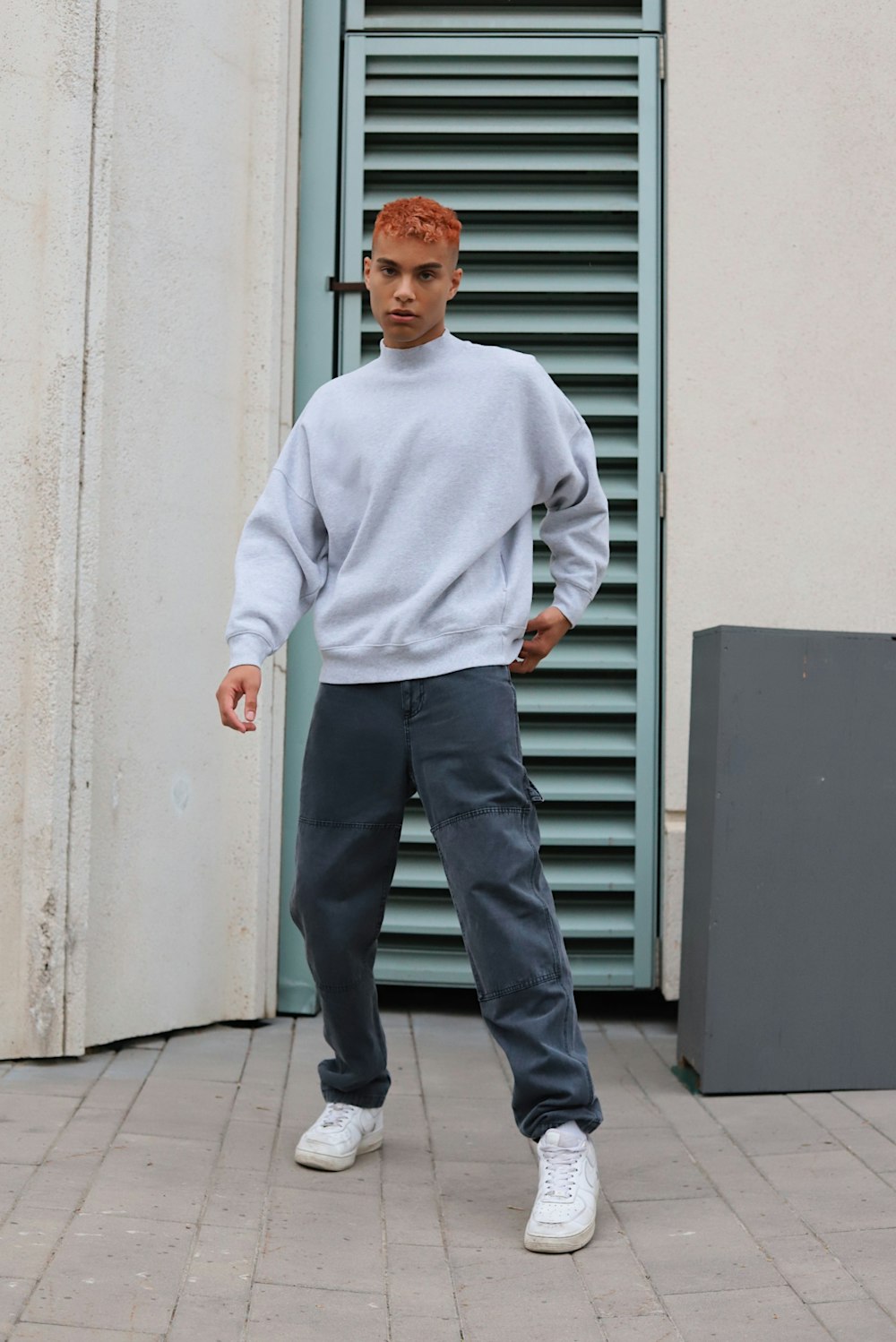 a man standing on a sidewalk wearing a sweater and sweatpants